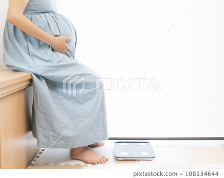 Pregnant woman sitting in front of weight scale 108134644