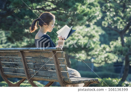 A woman reading a book on a park bench A woman reading a book on a park bench 108136399