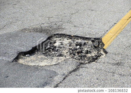 Damaged asphalt road with deep pothole on american highway surface. Ruined roadway in urgent need of repair 108136832