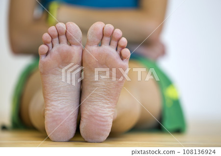 Close-up of woman sitting on the floor with bare feet. Legs care and skin treatment concept. Close-up of woman sitting on the floor with bare feet. Legs care and skin treatment concept. 108136924