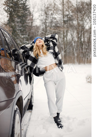 Young blonde woman standing near her car. Female model posing for a photo. Woman wearing black and white plaid shirt and grey sportive costume. Young blonde woman standing near her car. Female model posing for a photo. Woman wearing black and white plaid shirt and grey sportive costume. 108137450