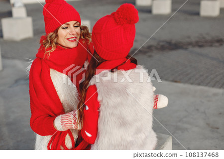 Mother and child in knitted winter hats on family Christmas vacation. Handmade wool hat and scarf for mom and kid. Knitting for kids. Knit outerwear. Woman and little girl in a park. 108137468
