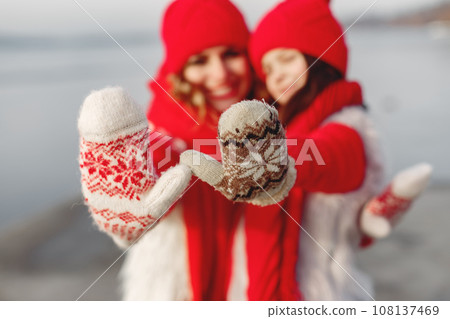Mother and child in knitted winter hats on family Christmas vacation. Handmade wool hat and scarf for mom and kid. Knitting for kids. Knit outerwear. Woman and little girl in a park. 108137469