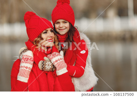 Mother and child in knitted winter hats on family Christmas vacation. Handmade wool hat and scarf for mom and kid. Knitting for kids. Knit outerwear. Woman and little girl in a park. 108137500