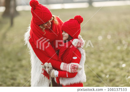 Mother and child in knitted winter hats on family Christmas vacation. Handmade wool hat and scarf for mom and kid. Knitting for kids. Knit outerwear. Woman and little girl in a park. 108137533