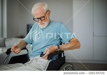 Senior man checking his blood sugar level on insulin pump. Close up of senior man in wheelchair with type 1 diabetes. 108139720