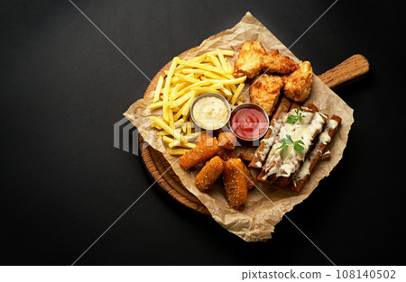 beer snacks - chicken fillet fried in batter with sauce on a wooden board on a black background beer snacks - chicken fillet fried in batter with sauce on a wooden board on a black background 108140502