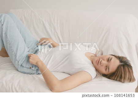 Cute asian woman zipping down her jean for her comfort lie on sofa in her home 108141653