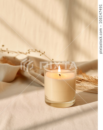 Minimalist burning wax candle in clear glass on natural beige stone background with copy space, styled commercial product mockup Minimalist burning wax candle in clear glass on natural beige stone background with copy space, styled commercial product mockup 108147491