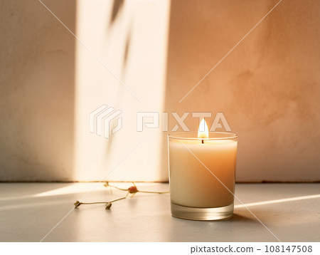 Minimalist burning wax candle in clear glass on natural beige stone background with copy space, styled commercial product mockup 108147508