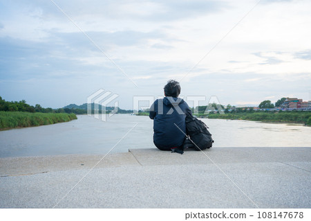 asian man sit and relax at side of river during sunset 108147678