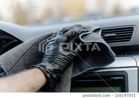 Man's hand in black glove cleaning car interior, dashboard and leather seats with microfiber cloth Man's hand in black glove cleaning car interior, dashboard and leather seats with microfiber cloth 108147831