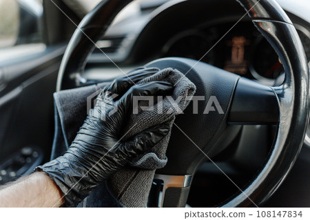 Man's hand in black glove cleaning car interior, dashboard and leather seats with microfiber cloth 108147834