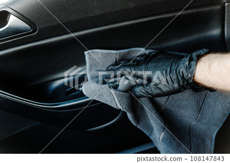 Man's hand in black glove cleaning car interior, dashboard and leather seats with microfiber cloth 108147843