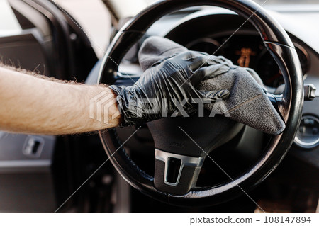 Man's hand in black glove cleaning car interior, dashboard and leather seats with microfiber cloth Man's hand in black glove cleaning car interior, dashboard and leather seats with microfiber cloth 108147894