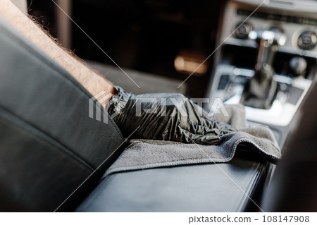 Man's hand in black glove cleaning car interior, dashboard and leather seats with microfiber cloth 108147908