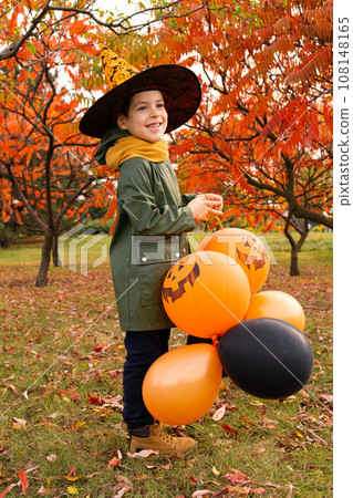 Happy Halloween kid playing with pumpkin balloons in park in autumn. 108148165