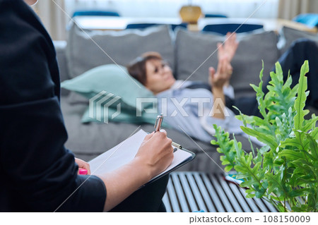 Close-up of female psychologist's hands with clipboard making notes, in therapy Close-up of female psychologist's hands with clipboard making notes, in therapy 108150009