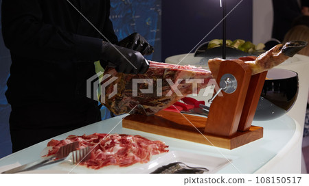 Sliced dried chamon prosciutto. A man cuts a jamon, a warm toned image. Selective focus point. 108150517