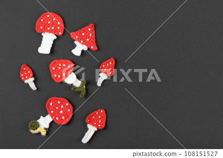 Knitted toys mushrooms fly agaric on a black background. Baby stuff and accessories. Halloween greeting card mockup with copy space. Happy Halloween holiday concept. Top view, flat lay, banner. 108151527