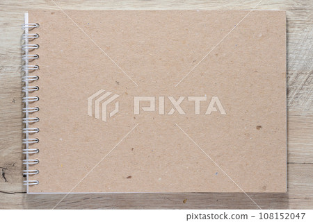 Spiral notepad on a wooden table. The notebook has a rectangular shape and a cover made of craft paper. Spiral notepad on a wooden table. The notebook has a rectangular shape and a cover made of craft paper. 108152047