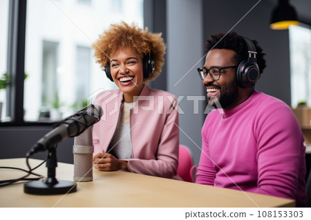 Beautiful multiethnic blogger couple hosting a podcast in a studio. Smiling woman and man wearing headphones sitting at a table with microphones and chatting cheerfully. Modern media technologies. Beautiful multiethnic blogger couple hosting a podcast in a studio. Smiling woman and man wearing headphones sitting at a table with microphones and chatting cheerfully. Modern media technologies. 108153303