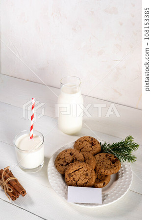 Cookies, milk, blank note, white wooden table, white wall. Christmas tradition - Milk for Santa. Cookies, milk, blank note, white wooden table, white wall. Christmas tradition - Milk for Santa. 108153385