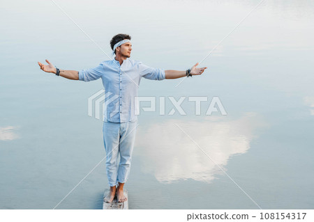 Man handsome stands on wooden bridge and looks at the water reflex of blue sky flinging his hands to the side. Concept of freedom relaxation. Place for text or advertising 108154317