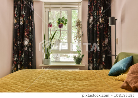 a bed with yellow comforter and pillows in front of a large window that looks out to the garden outside a bed with yellow comforter and pillows in front of a large window that looks out to the garden outside 108155185
