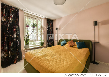 a bedroom with pink walls and yellow bedspremed bed in front of the window looking out onto the street 108155187
