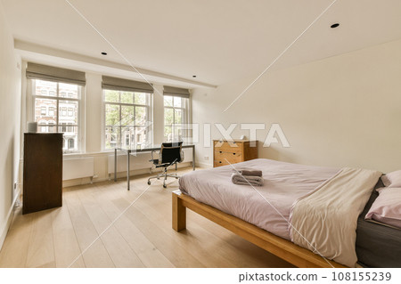 a bedroom with a bed, desk and tv in the corner of the room on the right is an open window 108155239