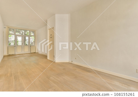 an empty living room with wood flooring and white walls, there is a large window to the left side an empty living room with wood flooring and white walls, there is a large window to the left side 108155261