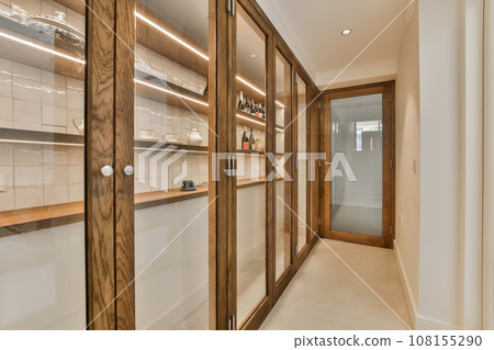 a long narrow hallway with wooden cabinets and white tiles on the walls, along with glass doors leading to another room a long narrow hallway with wooden cabinets and white tiles on the walls, along with glass doors leading to another room 108155290
