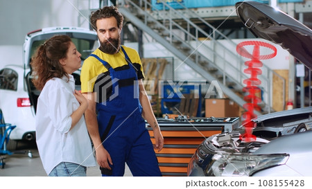 Repairman in repair shop using holographic augmented reality to show customer defective car piston. Seasoned garage professional using advanced AR tech to project automobile parts for woman 108155428