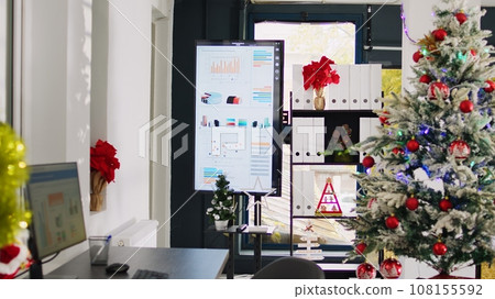 Dolly out shot of empty festive ornate office workspace with beautiful Christmas tree and pine wreaths. Xmas adorn professional workplace ready for festivities before winter holiday season vacation Dolly out shot of empty festive ornate office workspace with beautiful Christmas tree and pine wreaths. Xmas adorn professional workplace ready for festivities before winter holiday season vacation 108155592