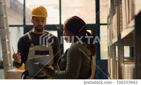 Team leader and worker performing warehouse inventory controls, keeping quality standards high. Trained experts in storage area preparing to ship parcels to customers, crosschecking delivery info 108155642