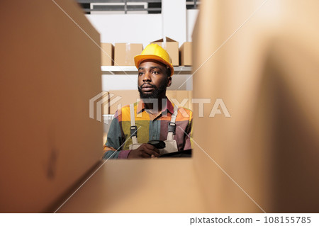 Selective focus of employee working in stockroom, scanning cardboard boxes using store scanner in warehouse. African american worker preparing customers order during storehouse inventory Selective focus of employee working in stockroom, scanning cardboard boxes using store scanner in warehouse. African american worker preparing customers order during storehouse inventory 108155785