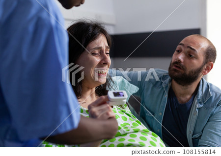 Nurse and husband comforting pregnant patient in hospital ward, having painful contractions. Womana with pregnancy getting into labor having medical assistance during checkup visit. Close up Nurse and husband comforting pregnant patient in hospital ward, having painful contractions. Womana with pregnancy getting into labor having medical assistance during checkup visit. Close up 108155814