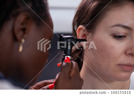 Otorhinolaryngologist in audiology hearing ear medical exam treating patient earache pain and infectious disease of ear canal. Doctor using otoscope during medical checkup in hospital. Close up. Otorhinolaryngologist in audiology hearing ear medical exam treating patient earache pain and infectious disease of ear canal. Doctor using otoscope during medical checkup in hospital. Close up. 108155818
