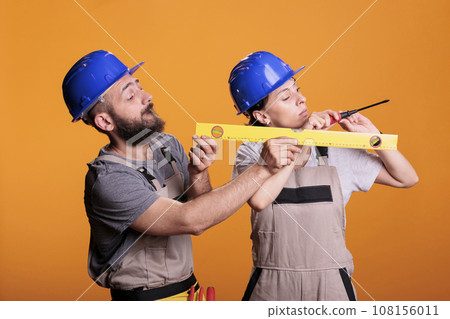 Contractors holding screwdriver and water level tool in studio shot, using ruler or leveler to work on renovation. Team of building experts being confident with renovating tools. 108156011