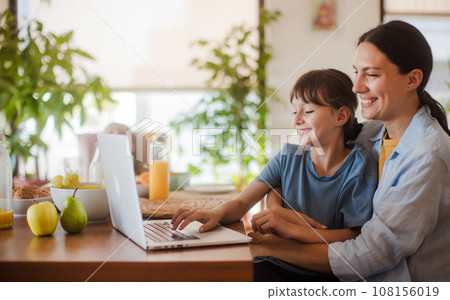 Mom and daughter watching entertaining videos on mom's work laptop. Remote work, home office for mothers with children. Mom and daughter watching entertaining videos on mom's work laptop. Remote work, home office for mothers with children. 108156019