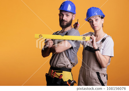 Construction workers holding screwdriver and water level in studio shot, using ruler or leveler to work on renovation. Team of building experts being confident with renovating tools. 108156076