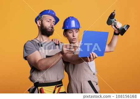 Team of construction workers analyzing papers on clipboard, taking notes of measurements. Builders looking at files with building or renovating information, engineering skills with power drill. 108156168