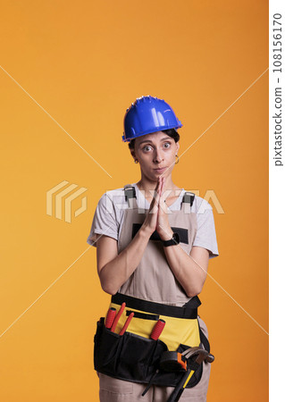 Female builder doing prayer hands sign on camera, begging and asking for new renovation projects. Woman construction worker hoping to work on building site and renovation project. 108156170