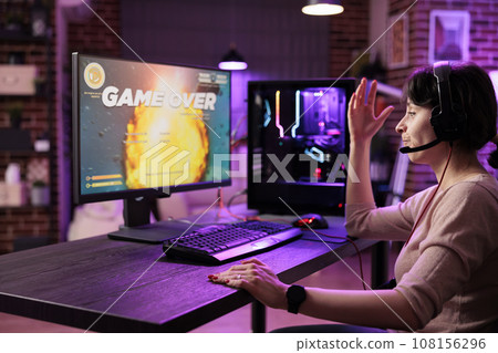 Frustrated gamer losing singleplayer spaceship arcade racing videogame, seeing game over screen on gaming computer display. Woman being dissapointed after being defeated on difficult game level Frustrated gamer losing singleplayer spaceship arcade racing videogame, seeing game over screen on gaming computer display. Woman being dissapointed after being defeated on difficult game level 108156296