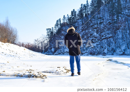 Man in warm clothes standing in the forest and looking at snowy mountains. winter, Russia. Man in warm clothes standing in the forest and looking at snowy mountains. winter, Russia. 108156412