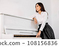 Beautiful woman dressed in white shirt playing on white piano. Place for text or advertising 108156836
