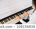 Beautiful woman dressed in white dress playing on white piano 108156838