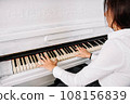 Beautiful woman dressed in white dress playing on white piano 108156839