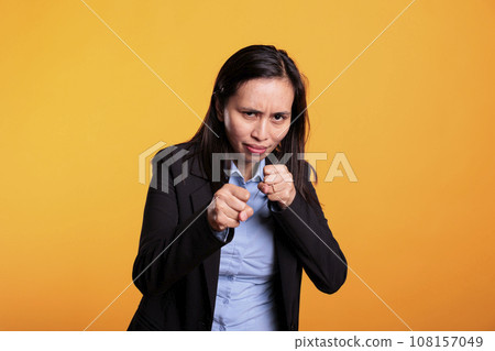Woman fighter clenching fists to punch in front of camera, preparing for boxing fight in studio. Strong filipino model having angry expression doing fighting gesture, shoowing defense strategy 108157049